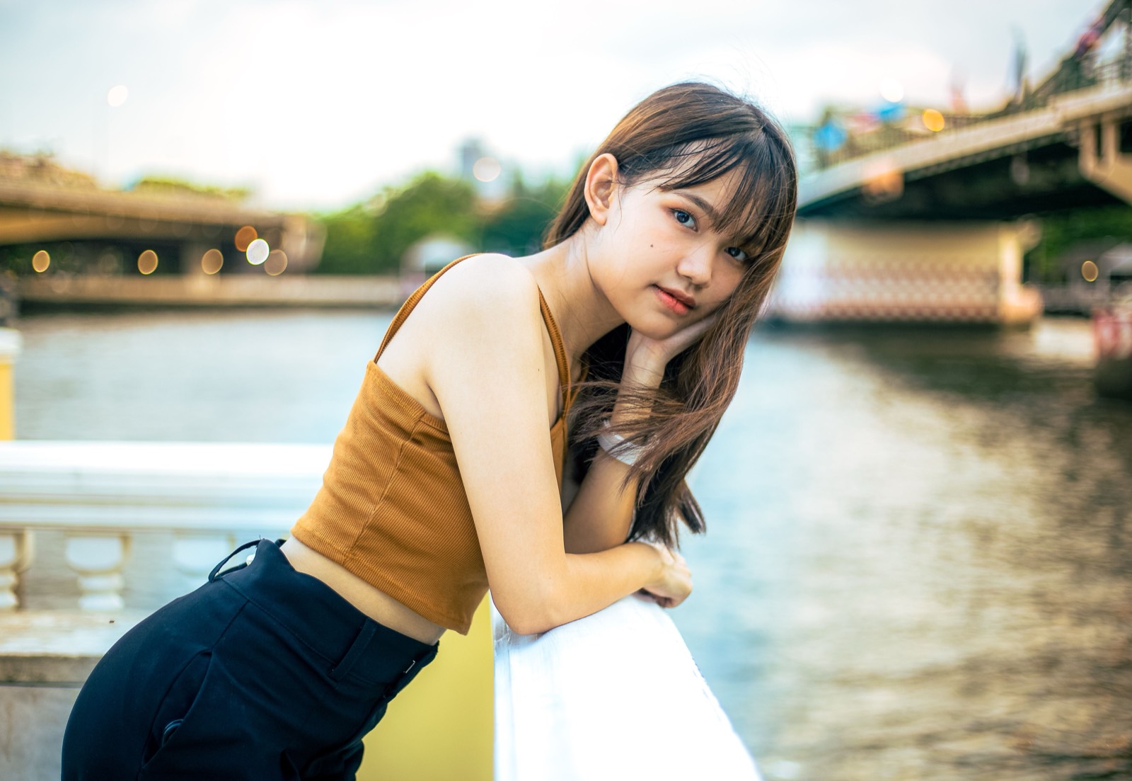 Thai woman in a mustard top by a riverfront railing
